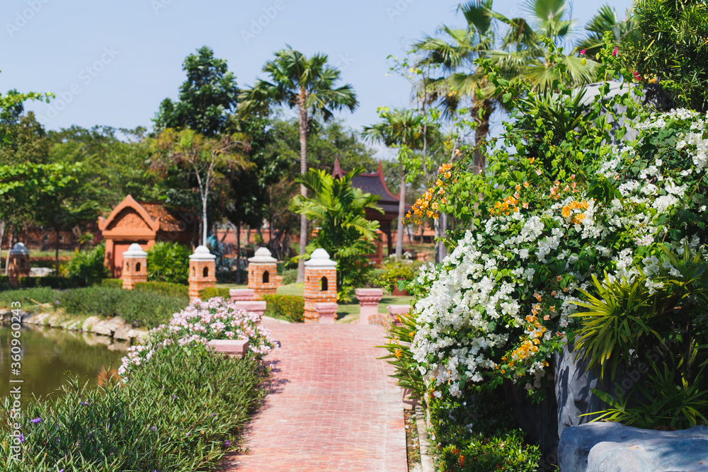 MUEANG BORAN, ANCIENT SIAM (ANCIENT CITY), SAMUT PRAKAN PROVINCE, BANGKOK, THAILAND - March 19, 2017 : Beautiful landscape with path, flowering bush and palm trees at park museum Muang Boran