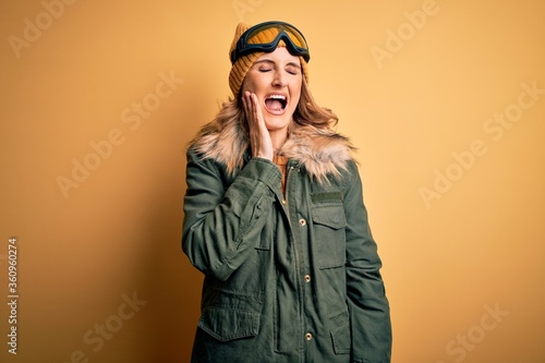 Middle age beautiful blonde skier woman wearing snow sportwear and ski goggles touching mouth with hand with painful expression because of toothache or dental illness on teeth. Dentist