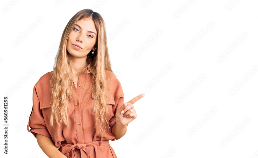Fototapeta premium Beautiful caucasian woman with blonde hair wearing summer jumpsuit pointing with hand finger to the side showing advertisement, serious and calm face