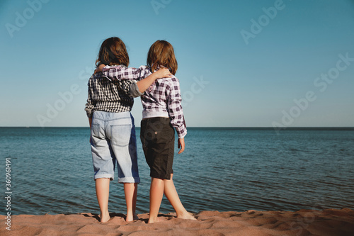 Two girls on the beach looking at the water. View from the back