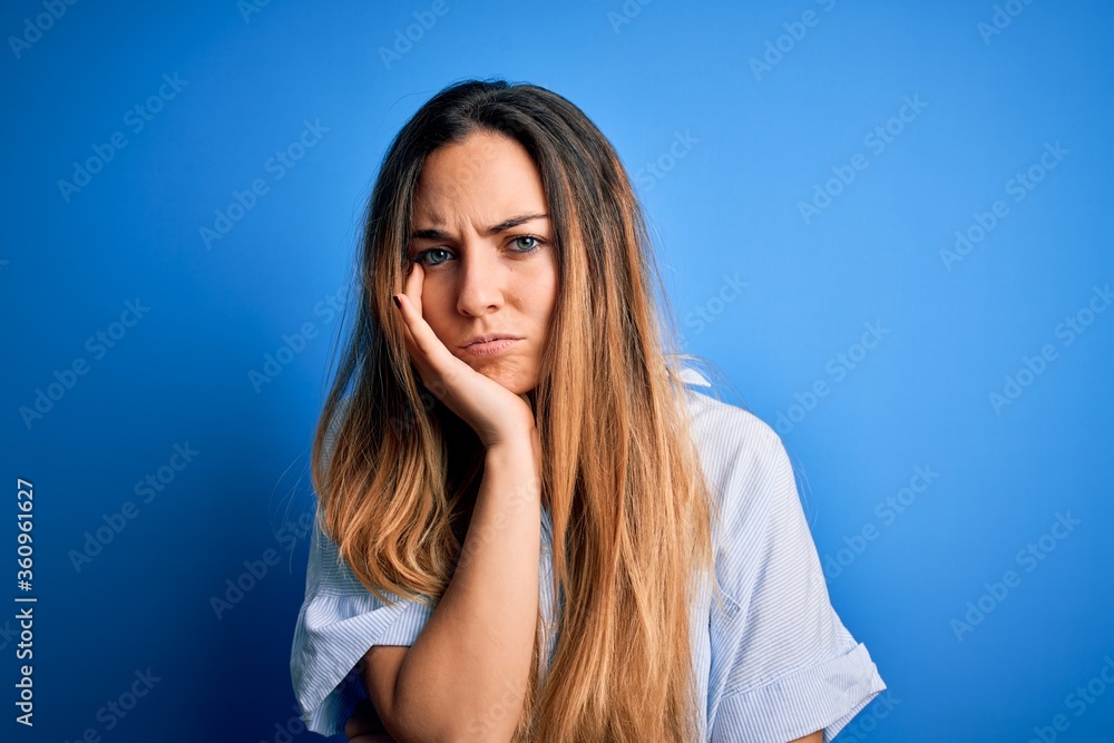 Young beautiful blonde woman with blue eyes wearing striped shirt over blue background thinking looking tired and bored with depression problems with crossed arms. Young beautiful blonde woman with blue eyes wearing striped shirt over blue background thinking looking tired and bored with depression problems with crossed arms.