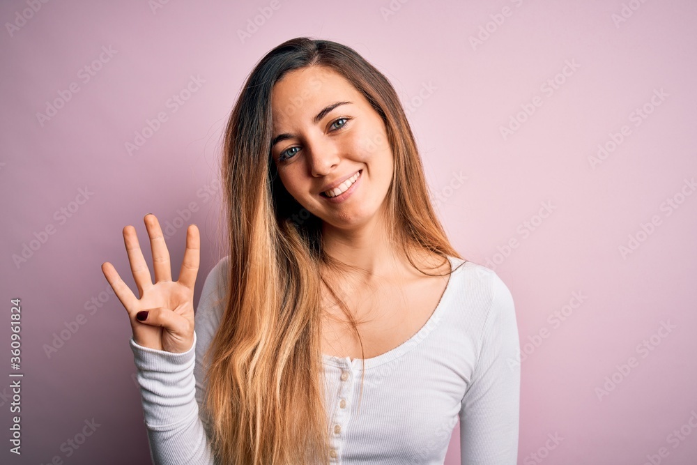 Young beautiful blonde woman with blue eyes wearing white t-shirt over pink background showing and pointing up with fingers number four while smiling confident and happy. Young beautiful blonde woman with blue eyes wearing white t-shirt over pink background showing and pointing up with fingers number four while smiling confident and happy.