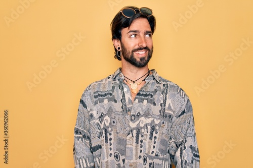 Young handsome hispanic bohemian man wearing hippie style and sunglasses looking away to side with smile on face, natural expression. Laughing confident.