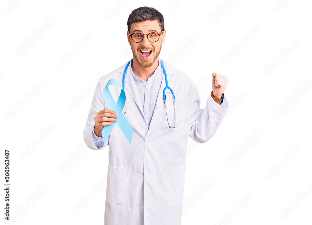 Handsome young man with bear wearing doctor uniform and holding blue ribbon screaming proud, celebrating victory and success very excited with raised arms Handsome young man with bear wearing doctor uniform and holding blue ribbon screaming proud, celebrating victory and success very excited with raised arms