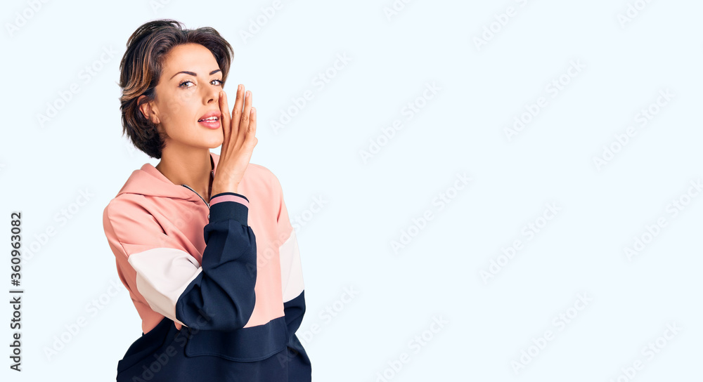 Young beautiful woman wearing sportswear hand on mouth telling secret rumor, whispering malicious talk conversation Young beautiful woman wearing sportswear hand on mouth telling secret rumor, whispering malicious talk conversation