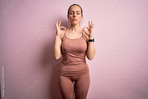 Young blonde fitness woman wearing sport workout clothes over pink isolated background relax and smiling with eyes closed doing meditation gesture with fingers. Yoga concept.