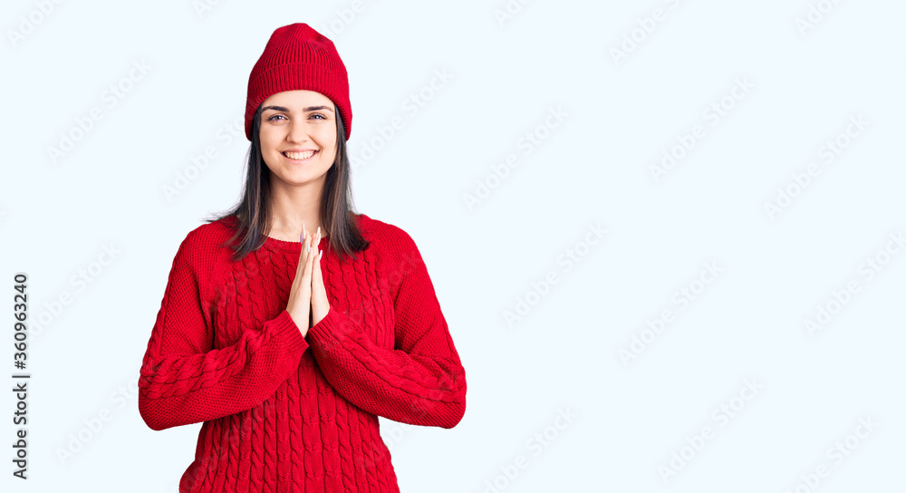 Young beautiful girl wearing sweater and wool cap praying with hands together asking for forgiveness smiling confident. Young beautiful girl wearing sweater and wool cap praying with hands together asking for forgiveness smiling confident.