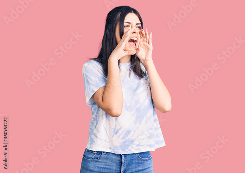 Young beautiful girl wearing casual t shirt shouting angry out loud with hands over mouth