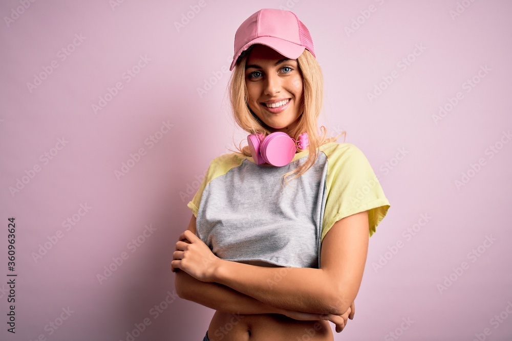 Young beautiful blonde sportswoman doing sport using headphones over pink background happy face smiling with crossed arms looking at the camera. Positive person. Young beautiful blonde sportswoman doing sport using headphones over pink background happy face smiling with crossed arms looking at the camera. Positive person.