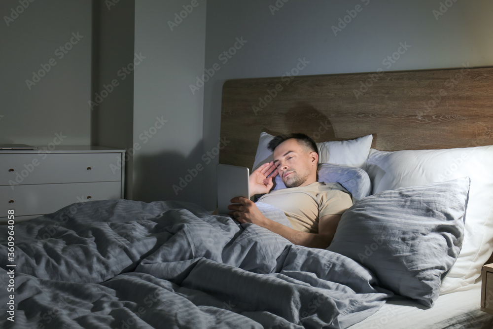 Young man suffering from sleep deprivation with tablet computer in bedroom at night Young man suffering from sleep deprivation with tablet computer in bedroom at night