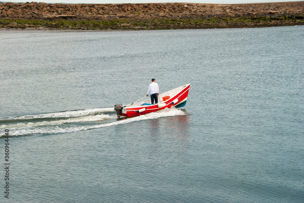 Fototapeta premium A man standing in a moving small red motorboat on a calm day