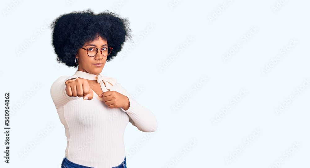 Young african american girl wearing casual clothes and glasses punching fist to fight, aggressive and angry attack, threat and violence Young african american girl wearing casual clothes and glasses punching fist to fight, aggressive and angry attack, threat and violence
