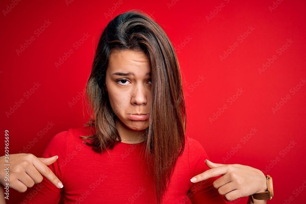 Young beautiful brunette girl wearing casual t-shirt over isolated red background Pointing down looking sad and upset, indicating direction with fingers, unhappy and depressed. Young beautiful brunette girl wearing casual t-shirt over isolated red background Pointing down looking sad and upset, indicating direction with fingers, unhappy and depressed.