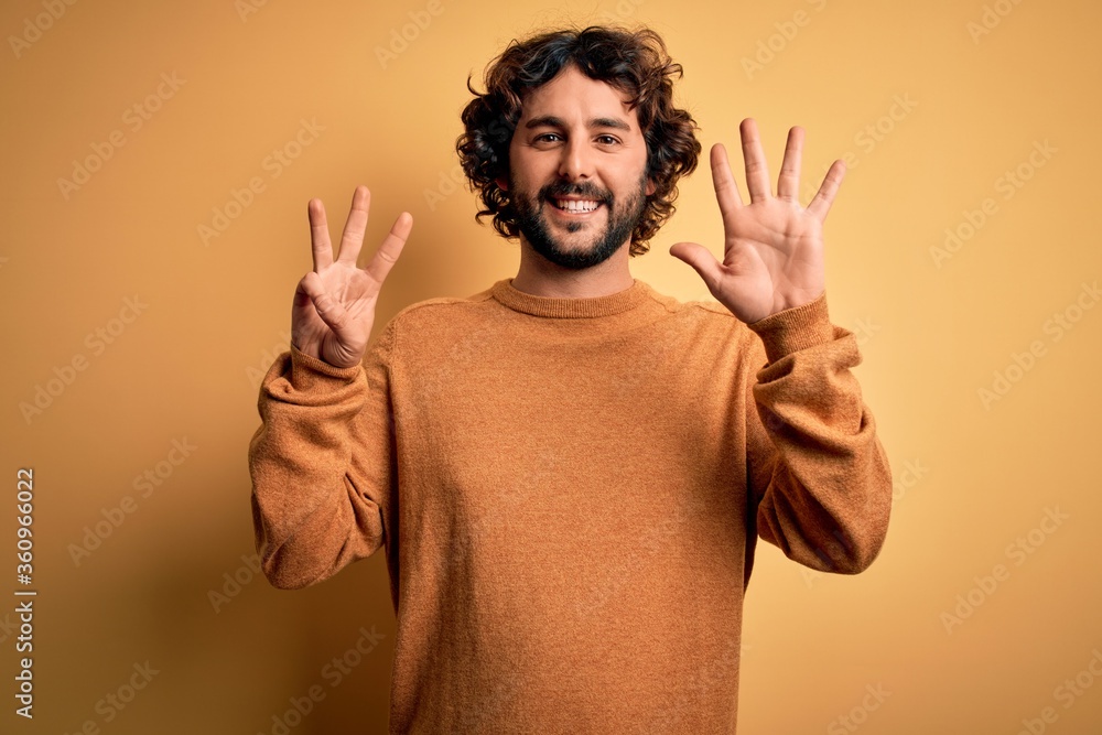 Young handsome man with beard wearing casual sweater standing over yellow background showing and pointing up with fingers number eight while smiling confident and happy. Young handsome man with beard wearing casual sweater standing over yellow background showing and pointing up with fingers number eight while smiling confident and happy.