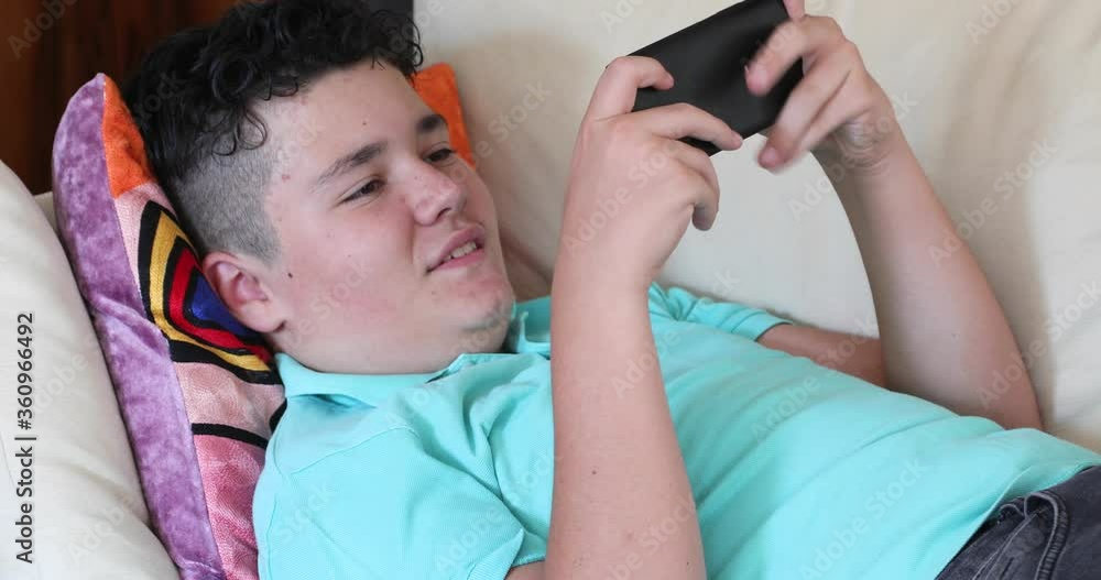 Portrait of a handsome teen boy sitting on coach alone Kid watching to screen, reading, typing, playing games. Technology, internet communication and people concept, Smartphone addiction Portrait of a handsome teen boy sitting on coach alone Kid watching to screen, reading, typing, playing games. Technology, internet communication and people concept, Smartphone addiction