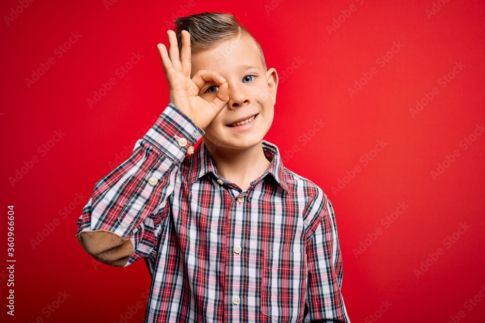 Young little caucasian kid with blue eyes standing wearing elegant shirt over red background doing ok gesture with hand smiling, eye looking through fingers with happy face. Young little caucasian kid with blue eyes standing wearing elegant shirt over red background doing ok gesture with hand smiling, eye looking through fingers with happy face.