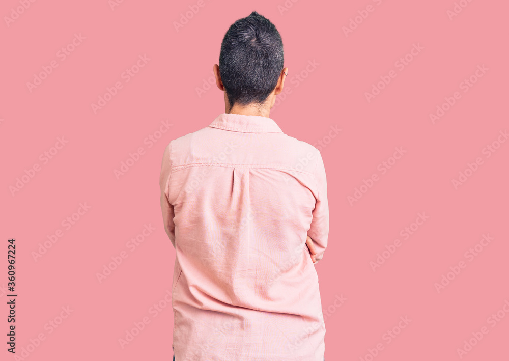 Young woman with short hair wearing casual clothes standing backwards looking away with crossed arms Young woman with short hair wearing casual clothes standing backwards looking away with crossed arms