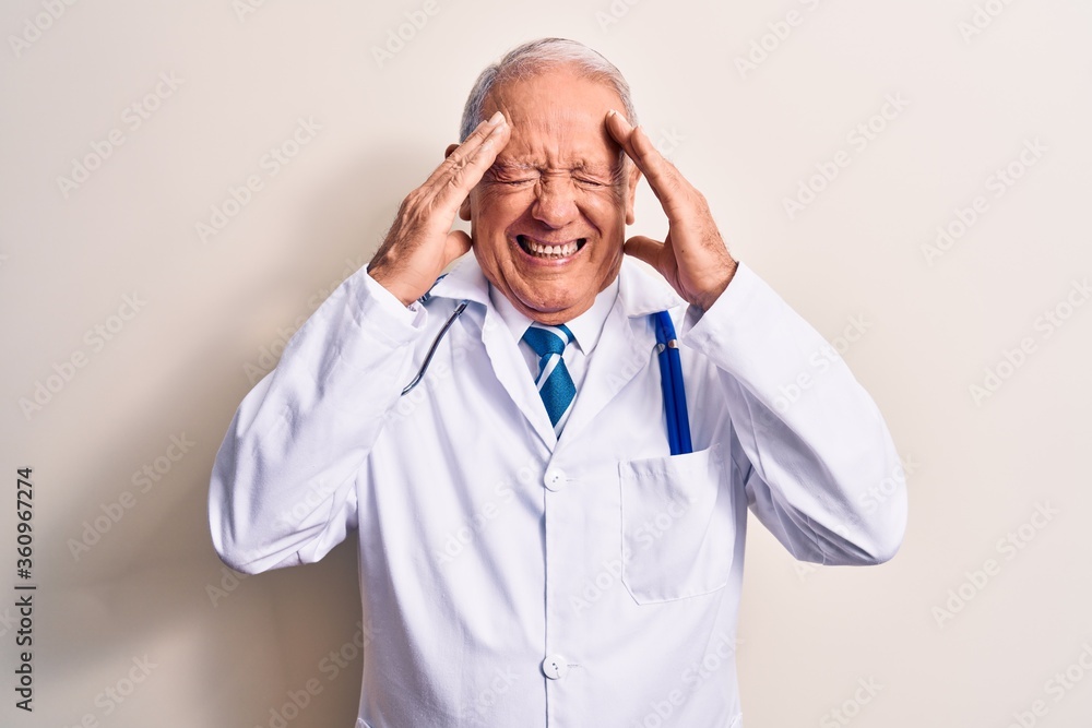 Senior grey-haired doctor man wearing coat and stethoscope standing over white background with hand on head, headache because stress. Suffering migraine. Senior grey-haired doctor man wearing coat and stethoscope standing over white background with hand on head, headache because stress. Suffering migraine.