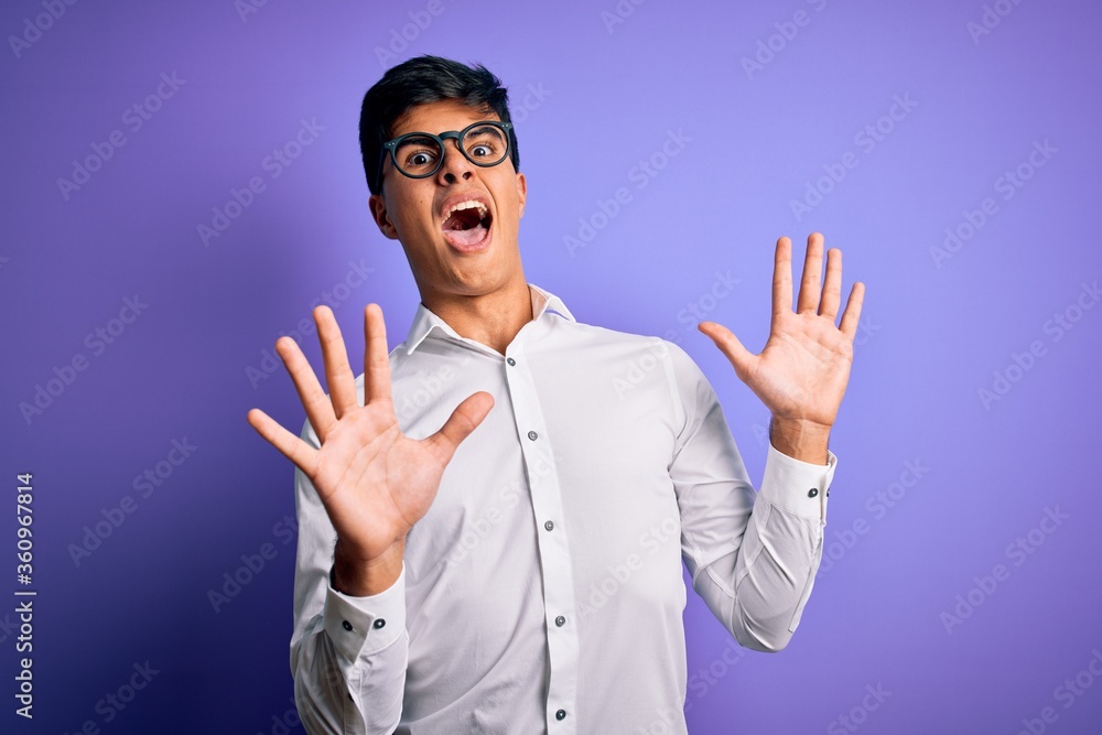 Young handsome business man wearing shirt and glasses over isolated purple background afraid and terrified with fear expression stop gesture with hands, shouting in shock. Panic concept. Young handsome business man wearing shirt and glasses over isolated purple background afraid and terrified with fear expression stop gesture with hands, shouting in shock. Panic concept.