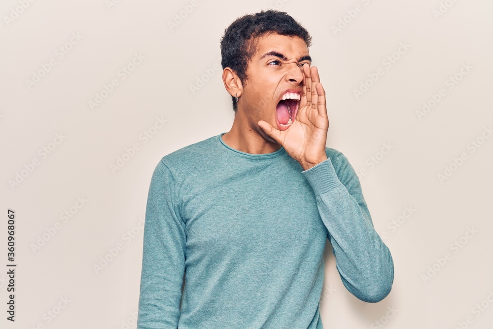 Young african amercian man wearing casual clothes shouting and screaming loud to side with hand on mouth. communication concept. Young african amercian man wearing casual clothes shouting and screaming loud to side with hand on mouth. communication concept.