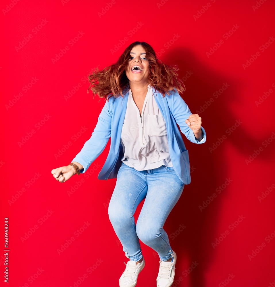 Young beautiful latin woman wearing casual clothes smiling happy. Jumping with smile on face doing winner gesture with fists up over isolated red background