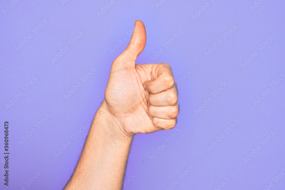 Hand of caucasian young man showing fingers over isolated purple background doing successful approval gesture with thumbs up, validation and positive symbol