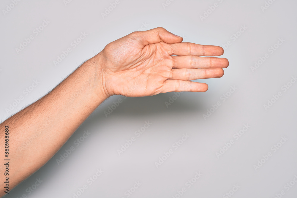 Hand of caucasian young man showing fingers over isolated white background stretching and reaching with open hand for handshake, showing palm Hand of caucasian young man showing fingers over isolated white background stretching and reaching with open hand for handshake, showing palm
