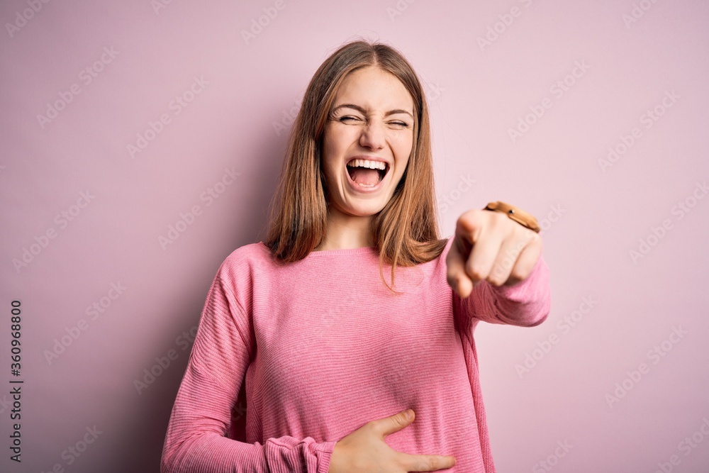 Young beautiful redhead woman wearing casual sweater over isolated pink background laughing at you, pointing finger to the camera with hand over body, shame expression Young beautiful redhead woman wearing casual sweater over isolated pink background laughing at you, pointing finger to the camera with hand over body, shame expression