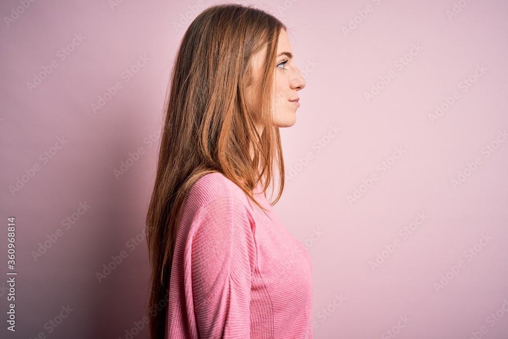Young beautiful redhead woman wearing casual sweater over isolated pink background looking to side, relax profile pose with natural face and confident smile. Young beautiful redhead woman wearing casual sweater over isolated pink background looking to side, relax profile pose with natural face and confident smile.