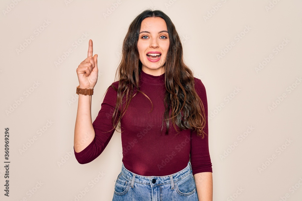 Young beautiful woman wearing casual t-shirt standing over isolated white background pointing finger up with successful idea. Exited and happy. Number one. Young beautiful woman wearing casual t-shirt standing over isolated white background pointing finger up with successful idea. Exited and happy. Number one.