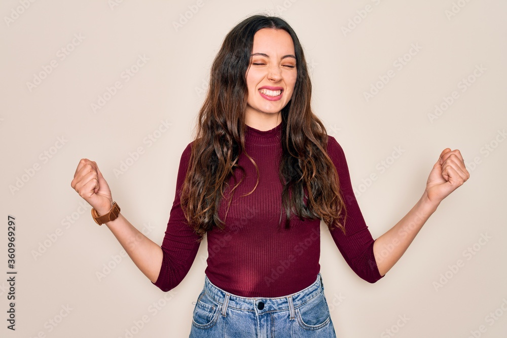 Young beautiful woman wearing casual t-shirt standing over isolated white background very happy and excited doing winner gesture with arms raised, smiling and screaming for success. Celebration Young beautiful woman wearing casual t-shirt standing over isolated white background very happy and excited doing winner gesture with arms raised, smiling and screaming for success. Celebration