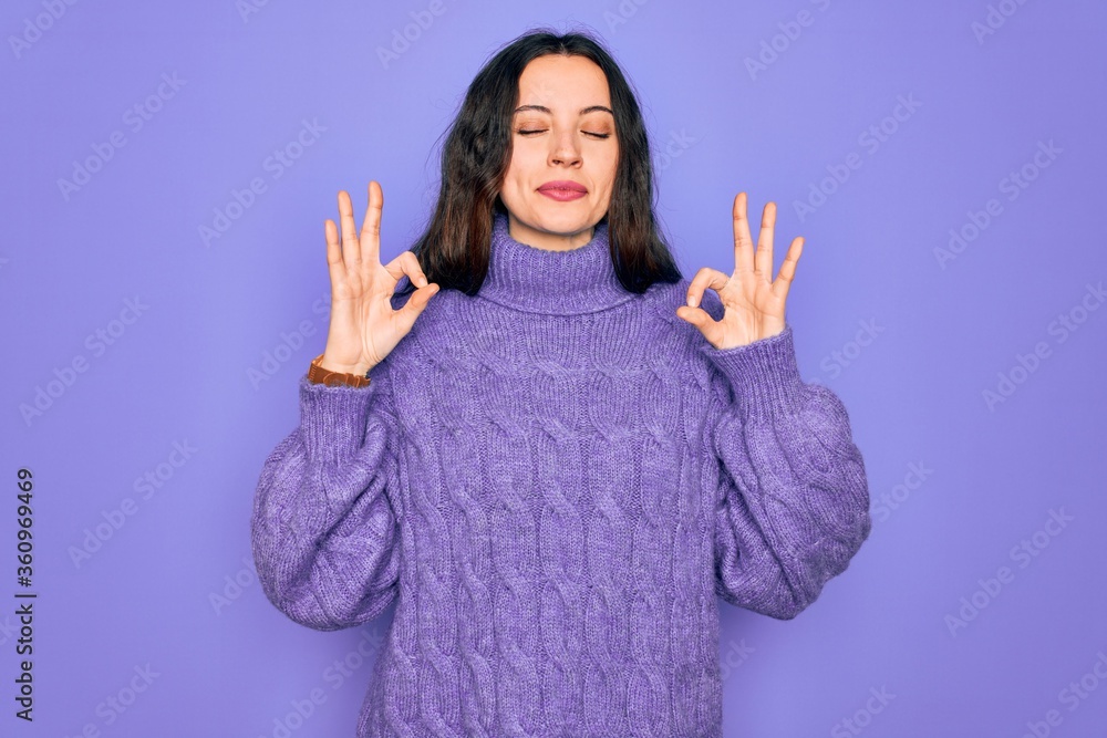 Young beautiful woman wearing casual turtleneck sweater standing over purple background relaxed and smiling with eyes closed doing meditation gesture with fingers. Yoga concept. Young beautiful woman wearing casual turtleneck sweater standing over purple background relaxed and smiling with eyes closed doing meditation gesture with fingers. Yoga concept.