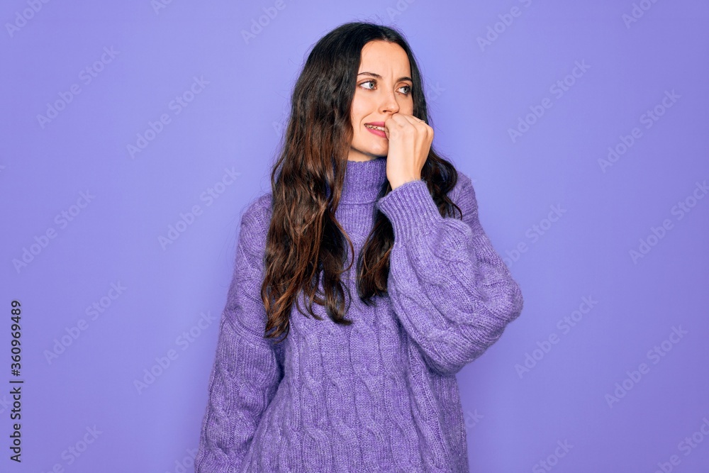 Young beautiful woman wearing casual turtleneck sweater standing over purple background looking stressed and nervous with hands on mouth biting nails. Anxiety problem. Young beautiful woman wearing casual turtleneck sweater standing over purple background looking stressed and nervous with hands on mouth biting nails. Anxiety problem.