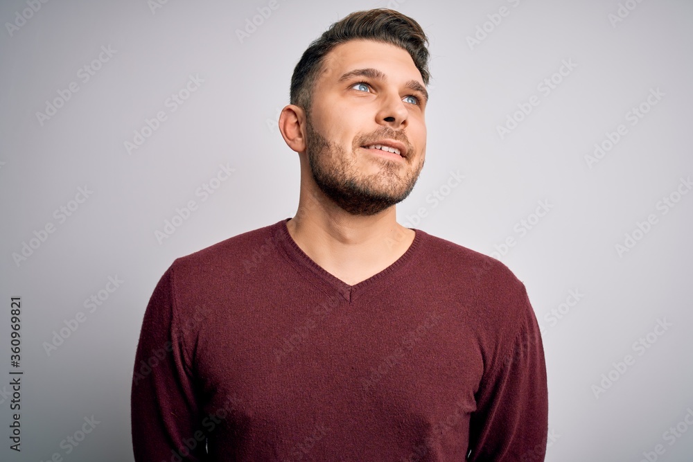 Fototapeta premium Young man with blue eyes wearing casual sweater standing over isolated background looking away to side with smile on face, natural expression. Laughing confident.