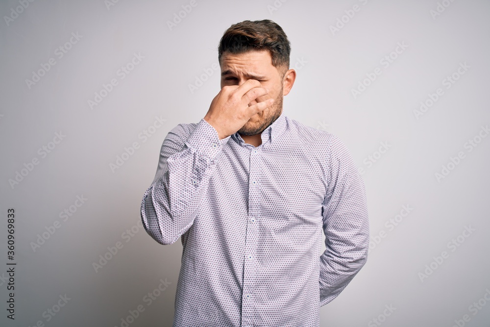 Young business man with blue eyes standing over isolated background smelling something stinky and disgusting, intolerable smell, holding breath with fingers on nose. Bad smell Young business man with blue eyes standing over isolated background smelling something stinky and disgusting, intolerable smell, holding breath with fingers on nose. Bad smell