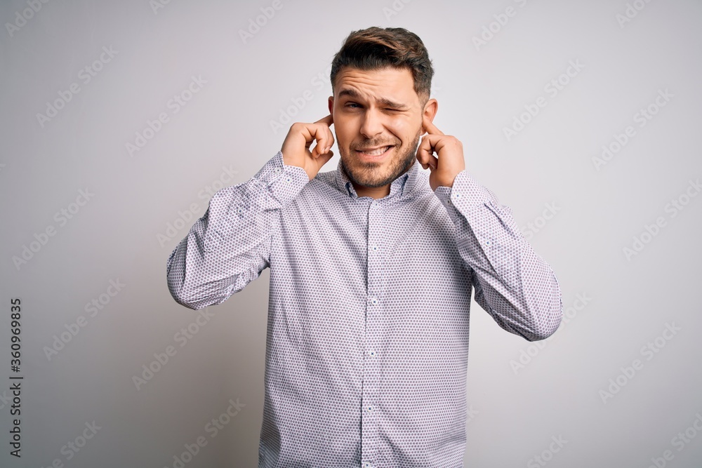 Young business man with blue eyes standing over isolated background covering ears with fingers with annoyed expression for the noise of loud music. Deaf concept. Young business man with blue eyes standing over isolated background covering ears with fingers with annoyed expression for the noise of loud music. Deaf concept.