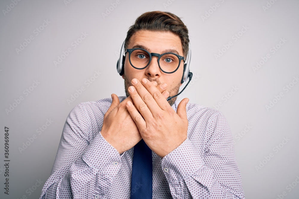 Young call center operator business man with blue eyes wearing glasses and headset shocked covering mouth with hands for mistake. Secret concept. Young call center operator business man with blue eyes wearing glasses and headset shocked covering mouth with hands for mistake. Secret concept.