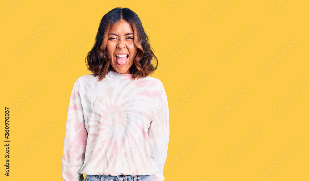 Obraz premium Young beautiful mixed race woman wearing casual tie dye sweatshirt sticking tongue out happy with funny expression. emotion concept.