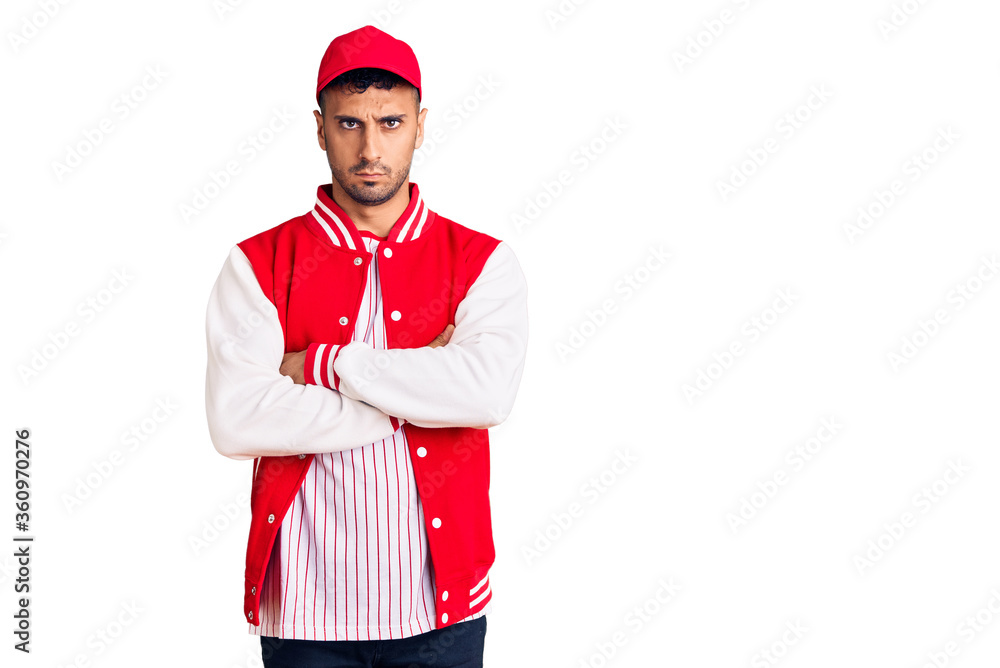 Young hispanic man wearing baseball uniform skeptic and nervous, disapproving expression on face with crossed arms. negative person. Young hispanic man wearing baseball uniform skeptic and nervous, disapproving expression on face with crossed arms. negative person.