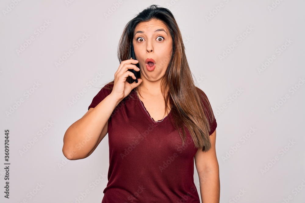 Fototapeta premium Young hispanic woman having a conversation talking on smartphone over isolated background scared in shock with a surprise face, afraid and excited with fear expression