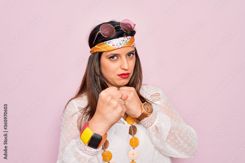 Young hispanic hippie woman wearing fashion boho style and sunglasses over pink background Ready to fight with fist defense gesture, angry and upset face, afraid of problem Young hispanic hippie woman wearing fashion boho style and sunglasses over pink background Ready to fight with fist defense gesture, angry and upset face, afraid of problem