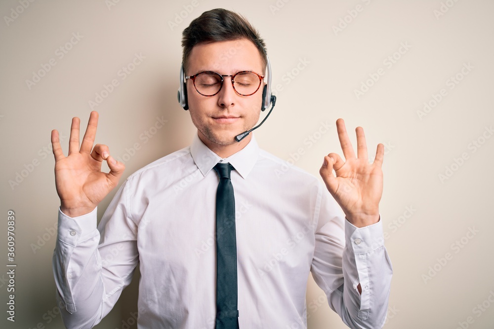 Young handsome caucasian business man wearing call center headset at customer service relax and smiling with eyes closed doing meditation gesture with fingers. Yoga concept. Young handsome caucasian business man wearing call center headset at customer service relax and smiling with eyes closed doing meditation gesture with fingers. Yoga concept.