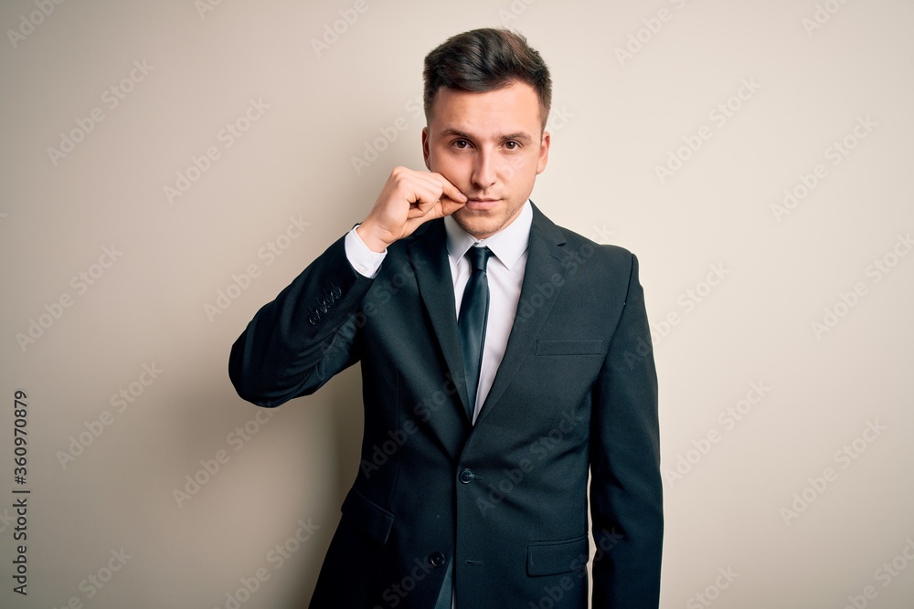 Young handsome business man wearing elegant suit and tie over isolated background mouth and lips shut as zip with fingers. Secret and silent, taboo talking Young handsome business man wearing elegant suit and tie over isolated background mouth and lips shut as zip with fingers. Secret and silent, taboo talking