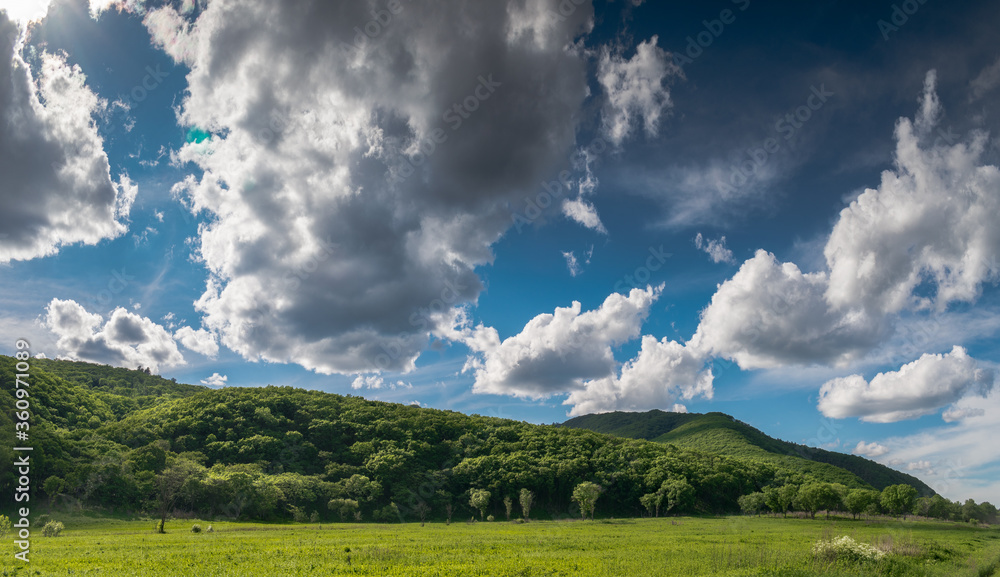 Summer landscape with green mountains and meadows, sky with clouds.
