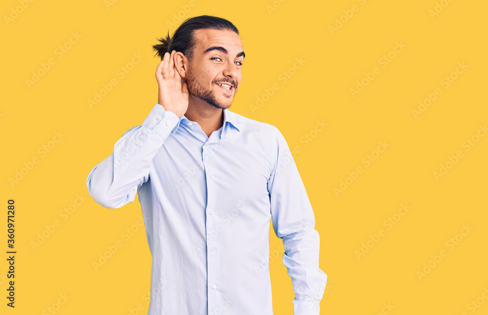 Young handsome man wearing business clothes smiling with hand over ear listening an hearing to rumor or gossip. deafness concept. Young handsome man wearing business clothes smiling with hand over ear listening an hearing to rumor or gossip. deafness concept.