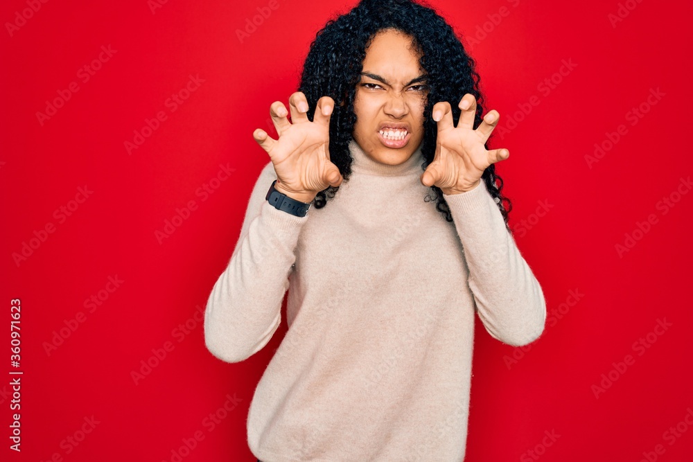 Young african american curly woman wearing casual turtleneck sweater over red background smiling funny doing claw gesture as cat, aggressive and sexy expression Young african american curly woman wearing casual turtleneck sweater over red background smiling funny doing claw gesture as cat, aggressive and sexy expression