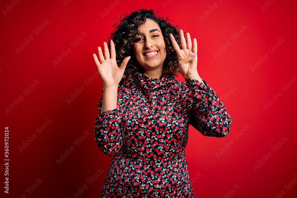 Young beautiful curly arab woman wearing casual floral dress standing over red background showing and pointing up with fingers number nine while smiling confident and happy. Young beautiful curly arab woman wearing casual floral dress standing over red background showing and pointing up with fingers number nine while smiling confident and happy.