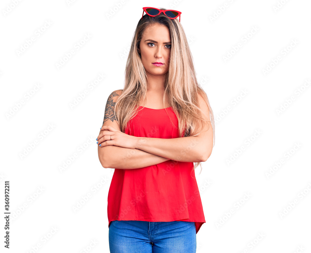 Young beautiful blonde woman wearing sleeveless t-shirt and sunglasses skeptic and nervous, disapproving expression on face with crossed arms. negative person. Young beautiful blonde woman wearing sleeveless t-shirt and sunglasses skeptic and nervous, disapproving expression on face with crossed arms. negative person.