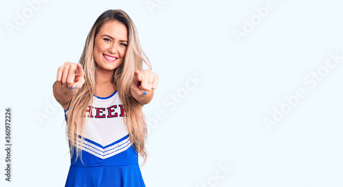 Young beautiful blonde woman wearing cheerleader uniform pointing to you and the camera with fingers, smiling positive and cheerful photo
