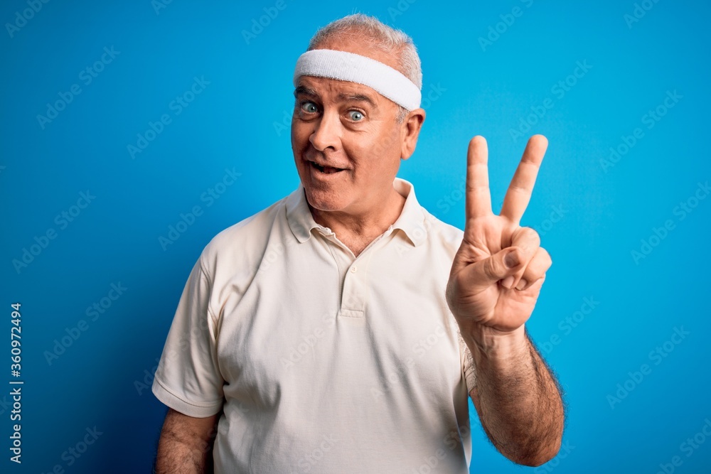 Middle age hoary sportsman doing sport wearing sportswear over isolated blue background showing and pointing up with fingers number two while smiling confident and happy.